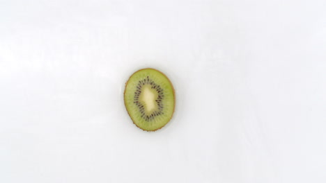 On-a-white-background-a-slice-of-kiwi-falls-into-the-water-with-a-splash.